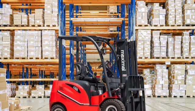 A red forklift positioned in front of large shelves filled with stacked boxes in a warehouse setting.