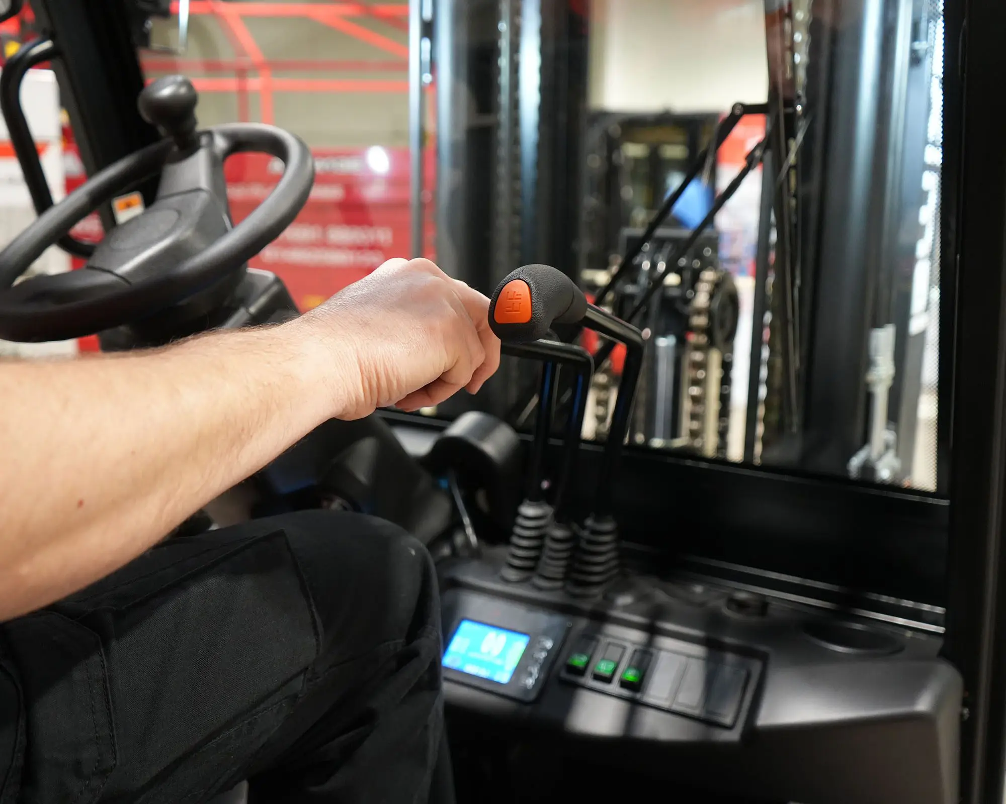 Close-up of a forklift operator's hand on the control lever inside a forklift cabin.
