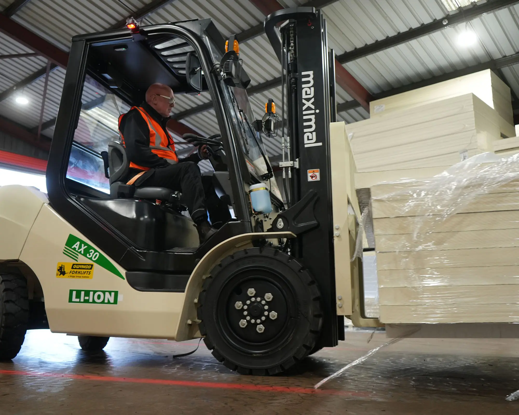A person operating an electric forklift to lift and transport stacked goods in a warehouse setting.