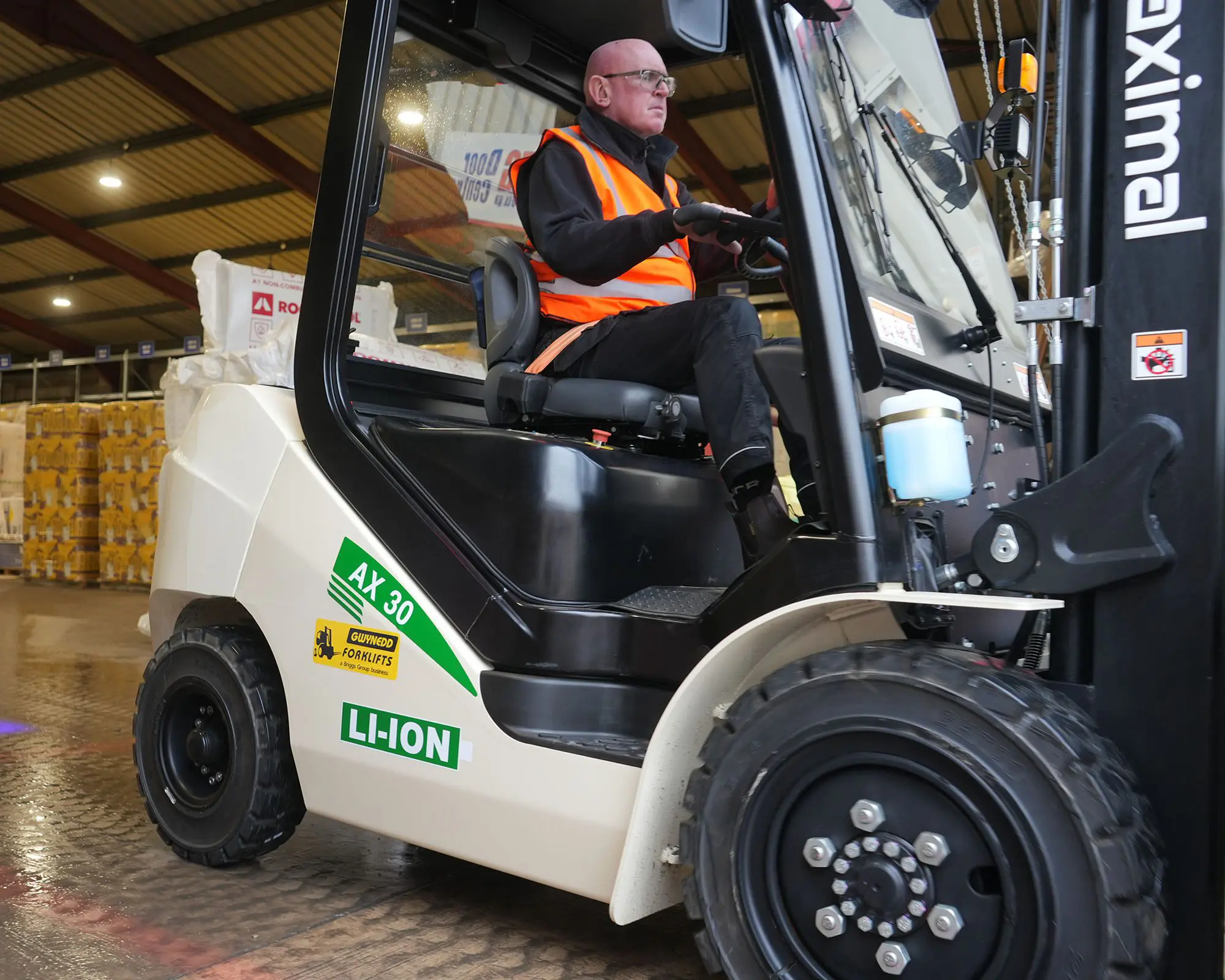 A person wearing a safety vest operating an electric forklift in a warehouse setting.