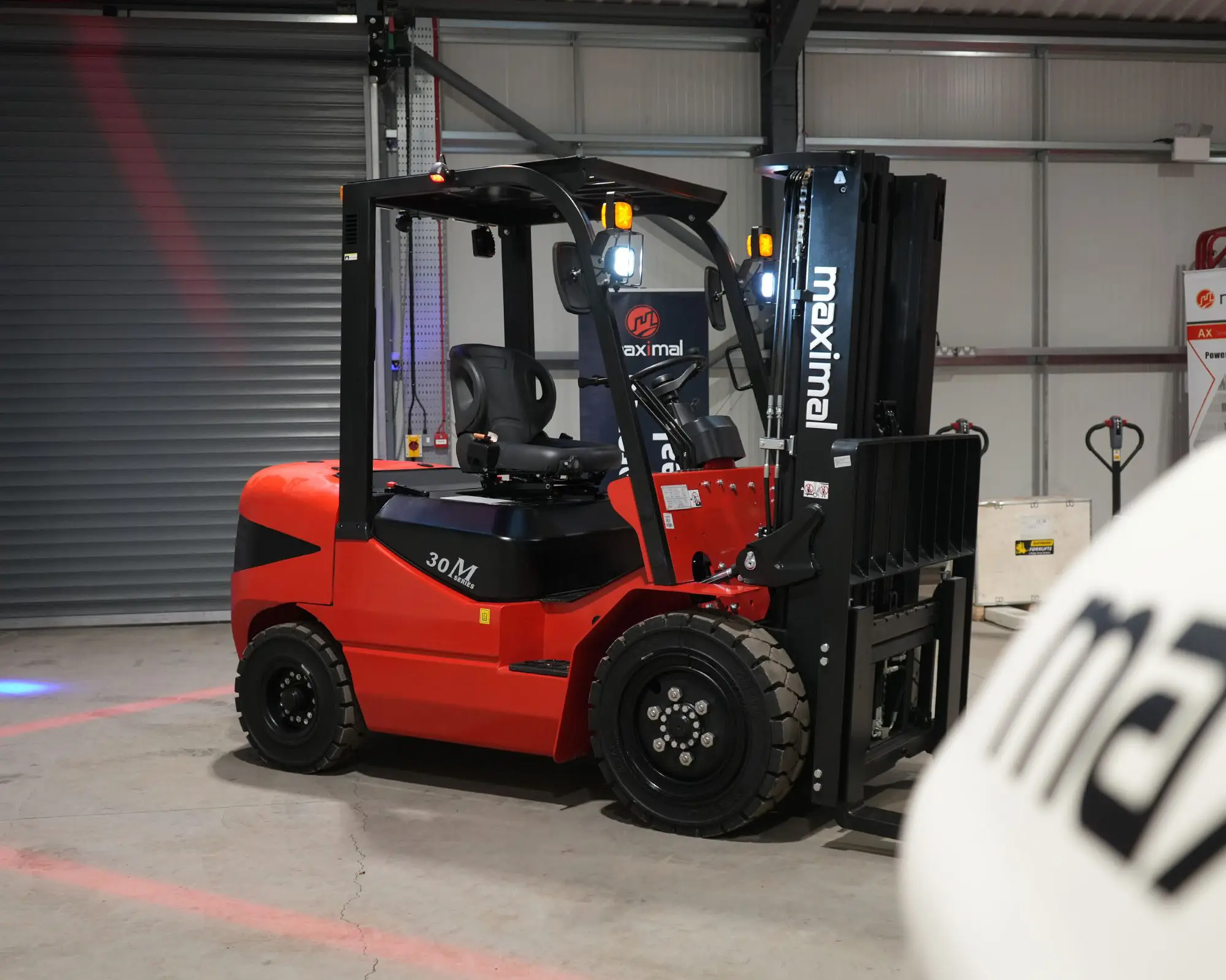 Maximal red forklift with raised fork in a warehouse setting, showcasing its design and functionality.