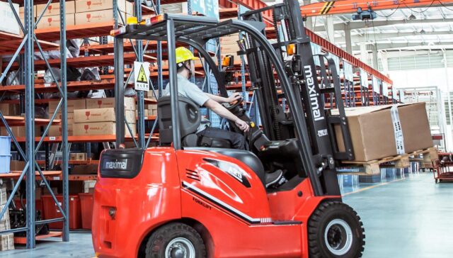 A worker operating a red forklift in a warehouse filled with shelves of boxes.