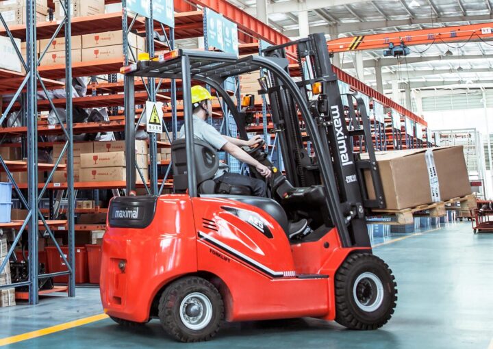 A worker operating a red forklift in a warehouse filled with shelves of boxes.