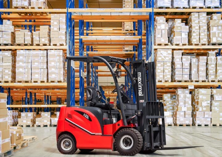 A red rear drive forklift positioned in front of large shelves filled with stacked boxes in a warehouse setting.