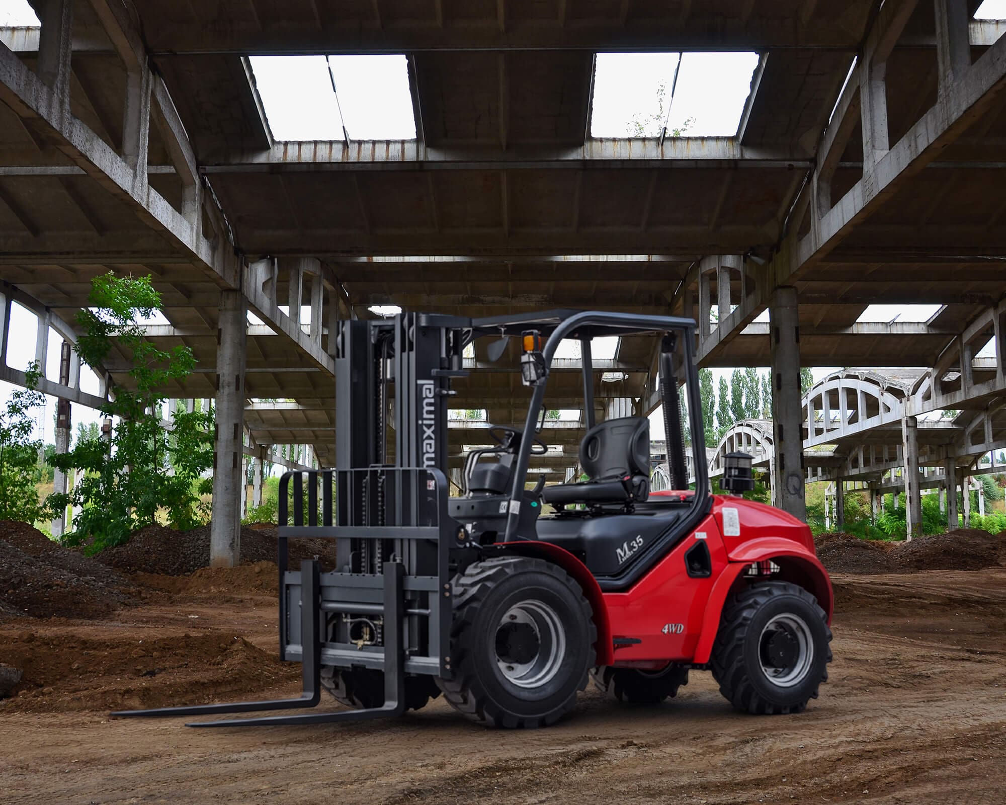 A robust red forklift parked on a dirt floor inside an industrial warehouse with large open windows and an unfinished structure.