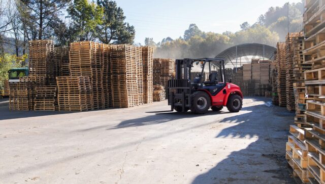 A red forklift navigating through a well-organized pallet storage facility under clear blue skies.