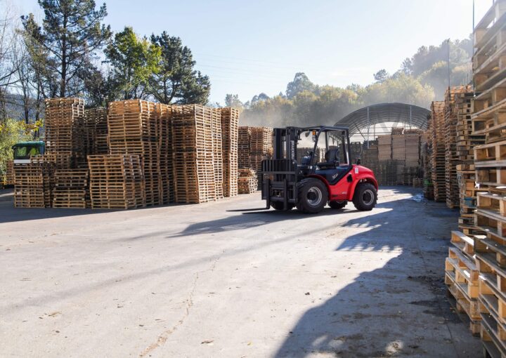 A red forklift navigating through a well-organized pallet storage facility under clear blue skies.