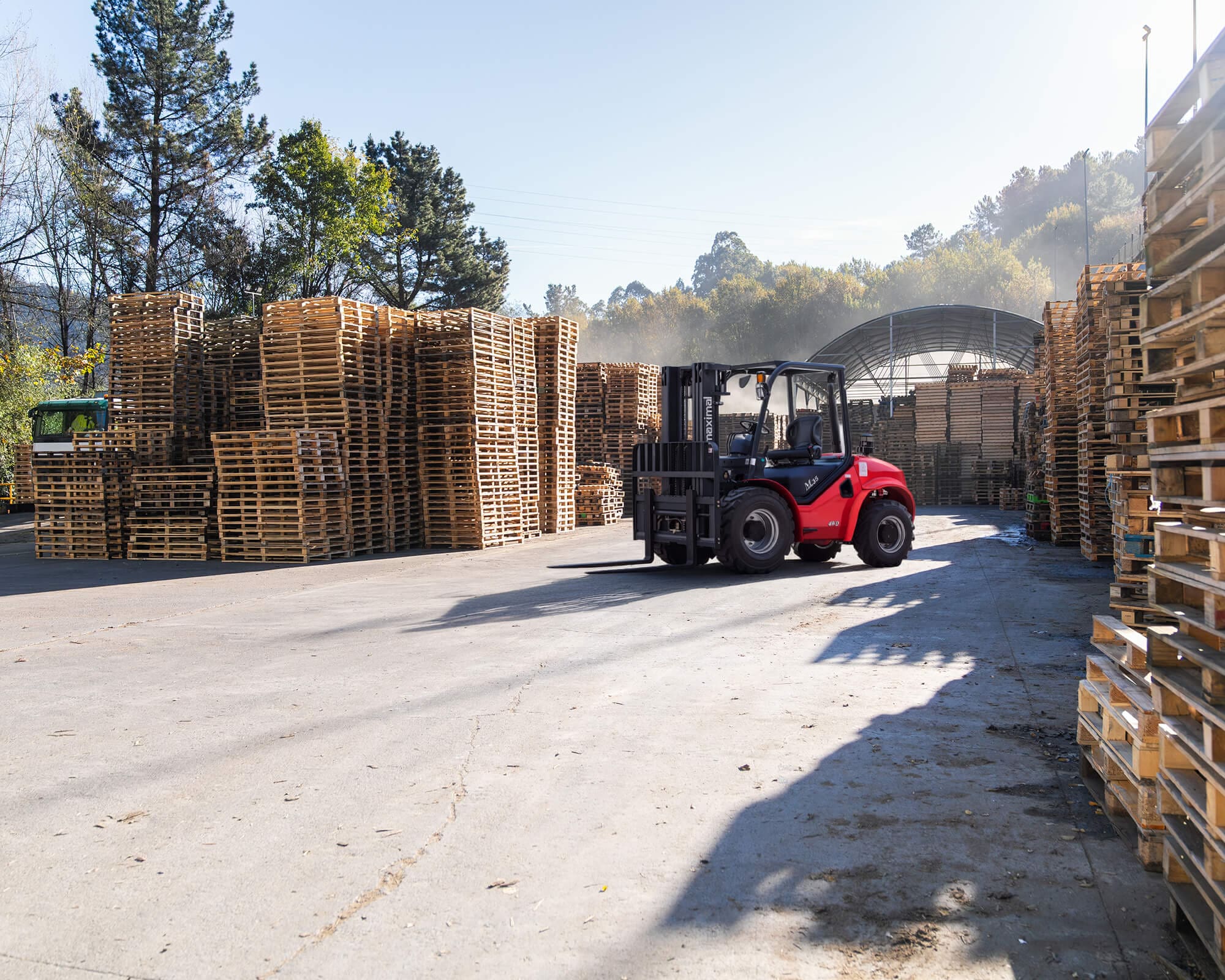 A red forklift navigating through a well-organized pallet storage facility under clear blue skies.