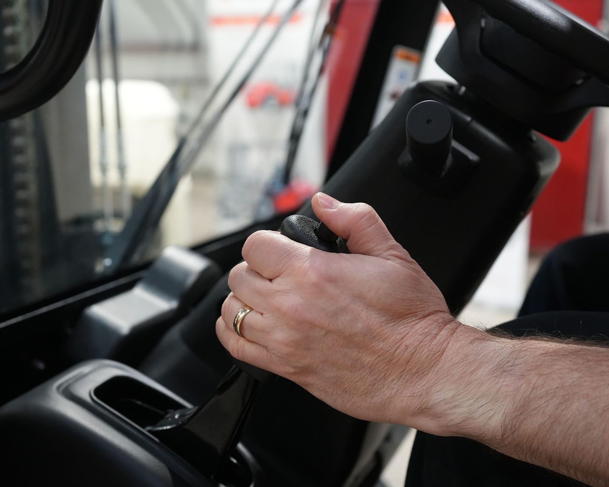 Operator Using Forklift Control Lever Close-up of a hand gripping the control lever of a forklift inside a warehouse setting.