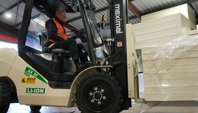 A person operating an electric forklift to lift and transport stacked goods in a warehouse setting.