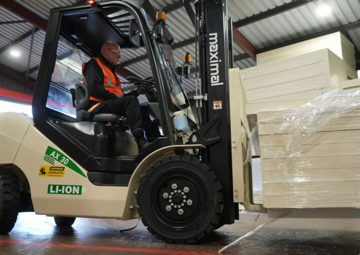 A person operating an electric forklift to lift and transport stacked goods in a warehouse setting.