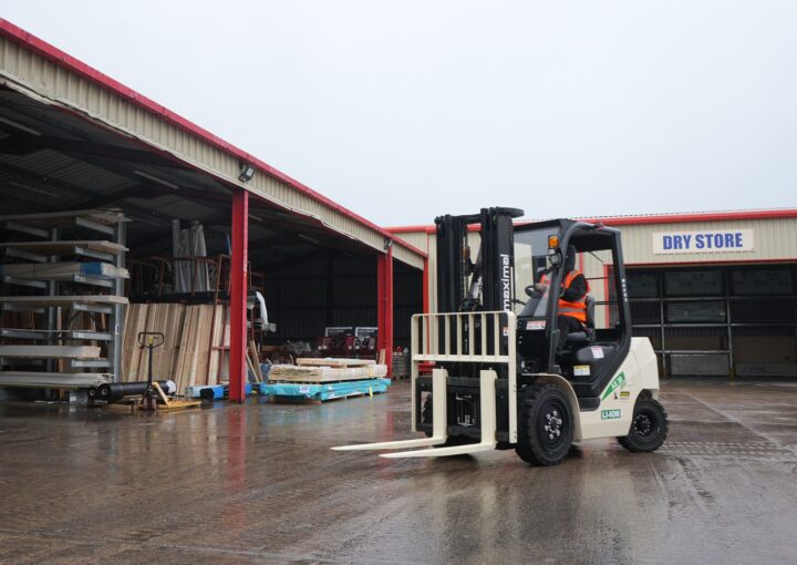 A forklift in operation outside a warehouse, surrounded by materials and equipment