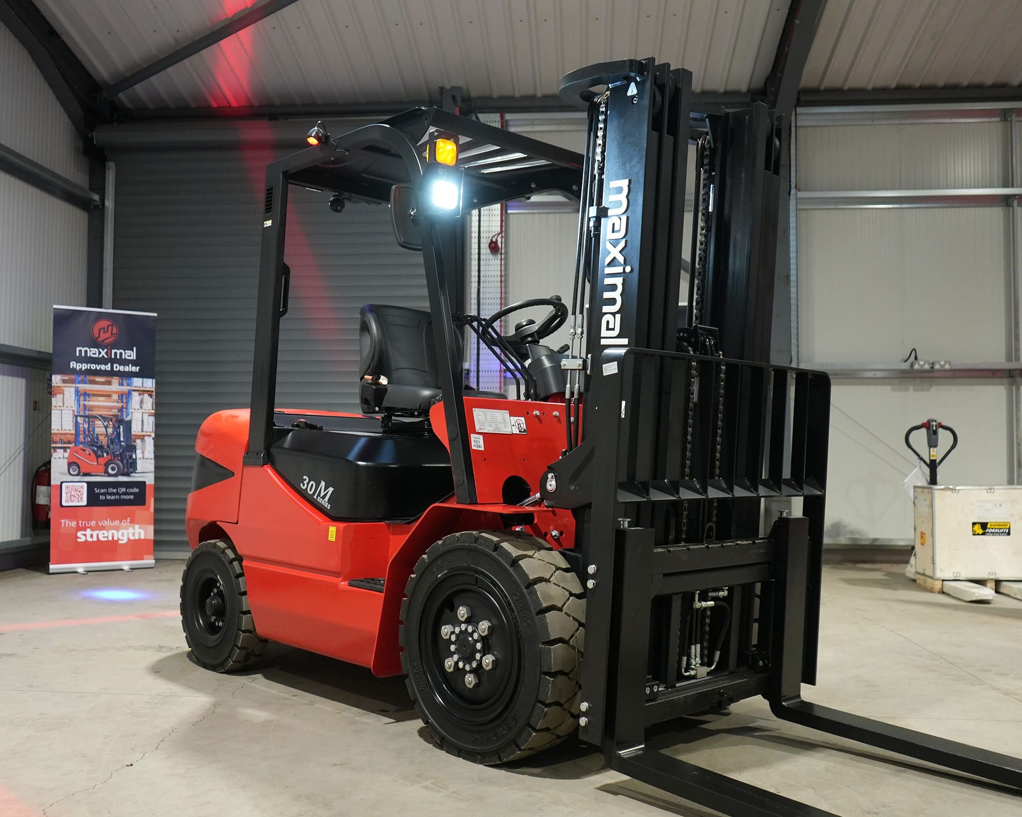 Red Maximal forklift parked inside a warehouse with cargo handling equipment in the background