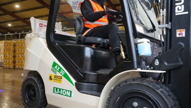 A person wearing a safety vest operating an electric forklift in a warehouse setting.
