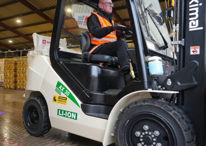A person wearing a safety vest operating an electric forklift in a warehouse setting.