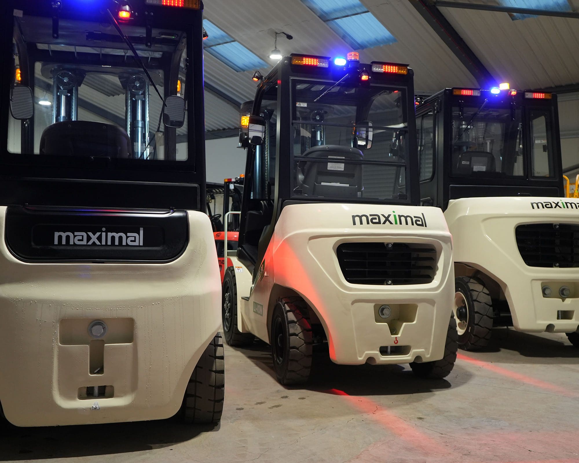 Three Maximal branded forklifts parked in a warehouse with lights on.